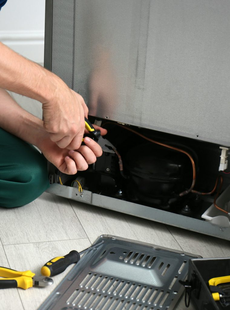 Male technician with pliers repairing refrigerator indoors, closeup